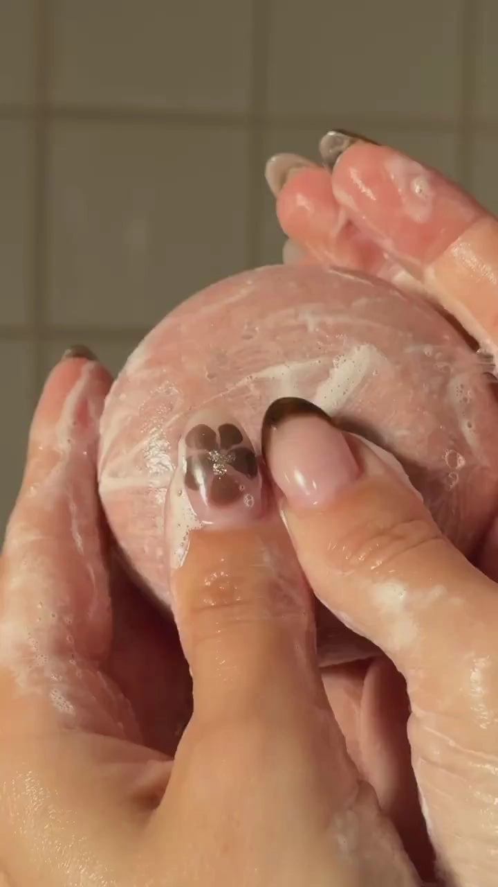 Hands working a pink shampoo bar into a lather