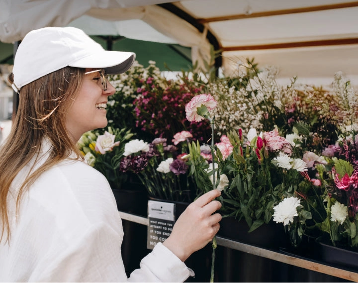 A smiling woman in a white cap holding a flower at a flower market