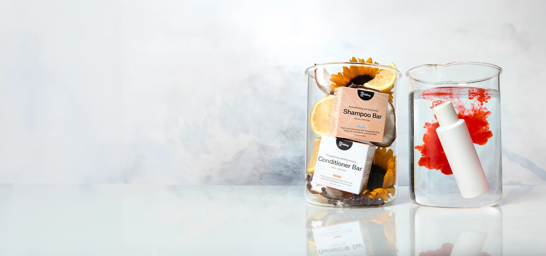 Shampoo bar and conditioner bar boxes in a glass beaker beside a second beaker of water