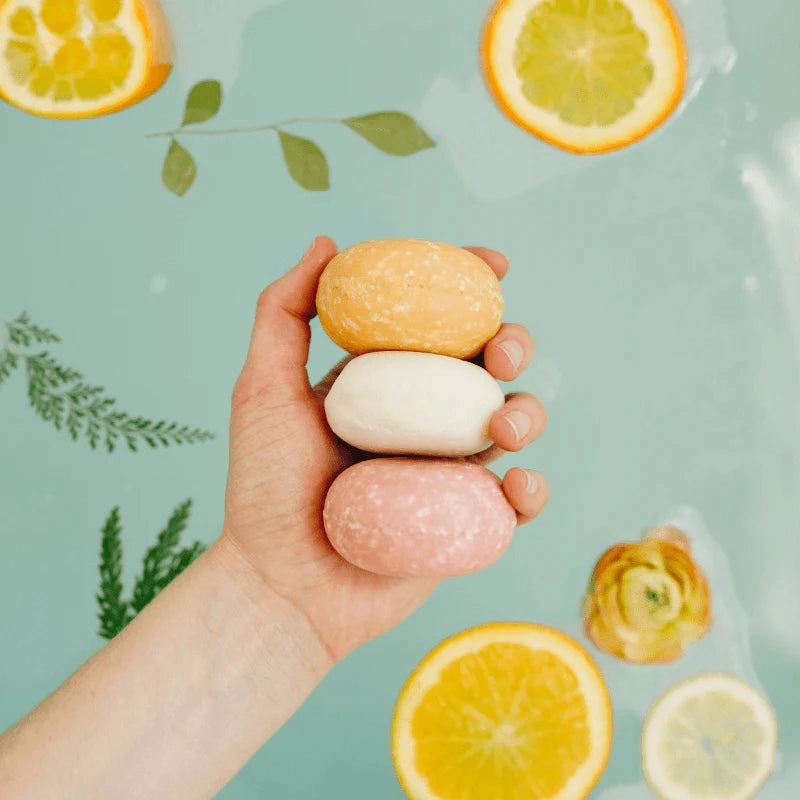 A hand holding three shampoo bars among citrus slices