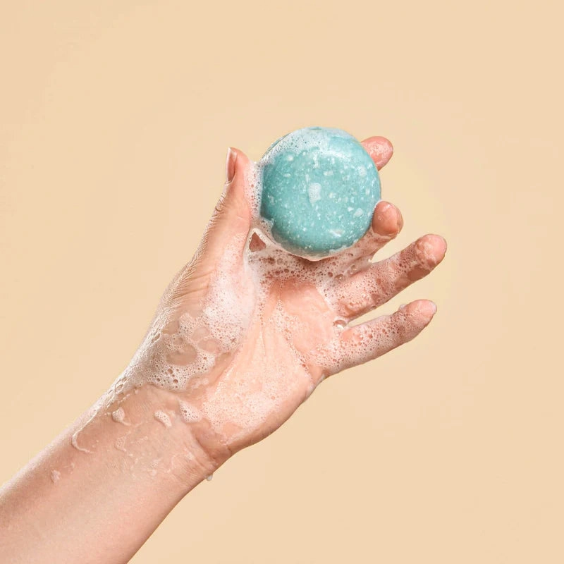 A hand holding a blue shampoo bar against a peach background