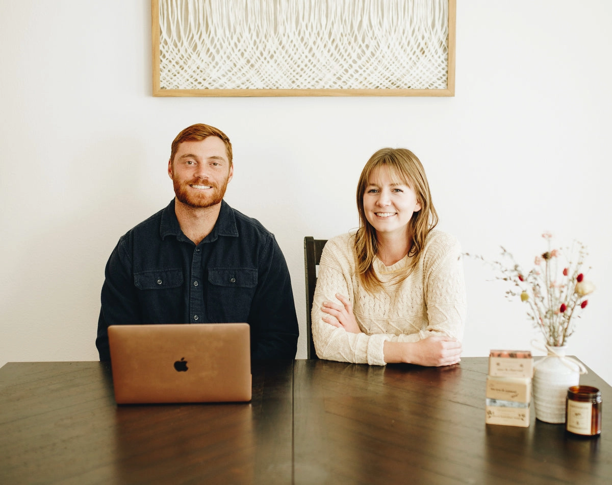 Two people seated at a dining table with a laptop and product bottles
